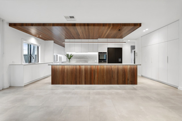 A renovated kitchen featuring clean white walls and cabinets, large light grey floor tiles, and feature wooden elements.